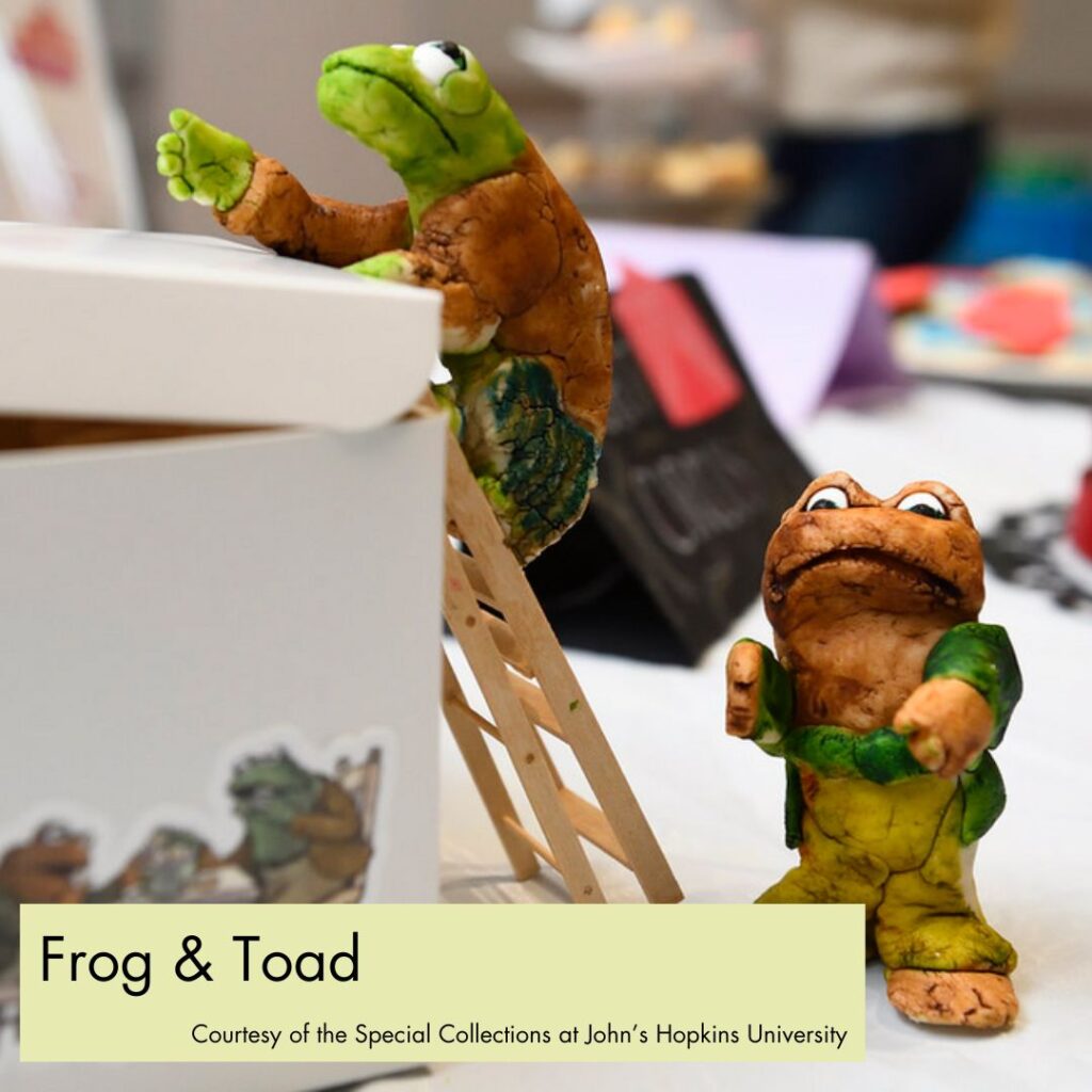 A photograph of children's book characters Frog and Toad, here made from fondant and food coloring. Frog is climbing a ladder while Toad stands next to the ladder. In the bottom right, a green rectangle overlays the picture with black text, reading "Frog & Toad, Courtesy of the Special Collections at John's Hopkins University."